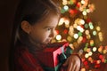 A child hugs a gift box in the twilight of Christmas night at a Christmas tree with colorful lights of garlands. Royalty Free Stock Photo