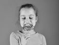 Child with hungry face poses with candy on green background. Treatment and sweets concept. Lady holds round shaped