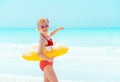 Child with inflatable lifebuoy pointing at something on beach