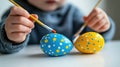 A child joyfully paints a blue and yellow egg using a brush, embracing the festive spirit of Easter. Royalty Free Stock Photo