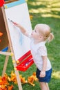 Child kid girl standing outside in summer autumn park drawing on easel with markers looking away playing studying