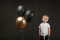 Child kid 3 years old, disappointed, skeptical, with balloons looking into camera on black background. Concept for birthday card