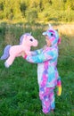 A child in kigurumi. A girl in a rainbow unicorn costume stands outside on a warm summer evening.