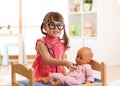 Child in kindergarten. Kid in nursery school. Little girl playing doctor with doll