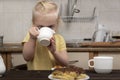 Child in the kitchen drinks from cup and looks at the cakes. Breakfast with child. Little girl drinking tea with pastry Royalty Free Stock Photo