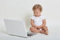 Child with lap top computer sitting on floor isolated over white background, kid wearing bodysuit, posing barefoot with note book Royalty Free Stock Photo