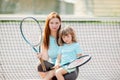 Child learning to play tennis with her mother on outdoor court. Little girl with tennis racket