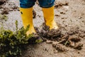 Child legs in yellow muddy rubber boots on wet mud. Baby playing with dirt at rainy weather.