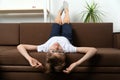 Child lies on couch with his head hanging down. Boy with glasses resting on sofa upside down