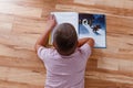 The child lies on his stomach on the floor and reads a big book