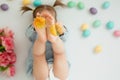 A child lies on a white background with Easter colored eggs and plays with yellow glasses.