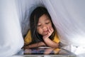 Child or Little girl hiding under the blanket using his smart phone or tablet with secret from her parents at night Royalty Free Stock Photo