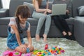 child a little girl is playing blocks at home. Mother with friend working on laptop or shopping online Royalty Free Stock Photo