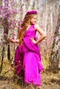 A child stands among the ledum and birch in a pink dress and smiling