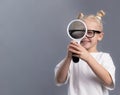 child smiling and looking through magnifying glass on gray background. Portrait of curious little girl holding magnifier, copy Royalty Free Stock Photo