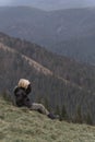 Child looks at the distance on vacation in mountain. Blond schoolboy sits at hillside. Vertical frame