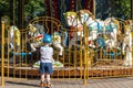 The child looks at old French carousel in a holiday park. Horses on a traditional fairground vintage carousel.