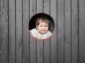 Child looks out of a round wooden window and smiles. The boy climbed out of the round window and smiles pretty straight into the Royalty Free Stock Photo