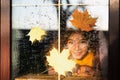 Child looks out of the window of the house outside, autumn weather, wet glass with drops after rain, yellow maple leaves stuck to Royalty Free Stock Photo