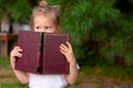 Child looks to side and holds book. The little girl is hiding behind book. Knowledge and learning Royalty Free Stock Photo