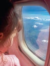 A child looks into the window of an plane. Little girl sees the blue sky and clouds in the window of an airplane. Baby flies on Royalty Free Stock Photo