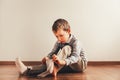 Child with lots of independence sitting on the floor putting on his socks with an expression of effort