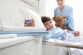 Child lying in bed in hospital room taking a pair of glasses with a nurse holding a teddy bear behind him Royalty Free Stock Photo