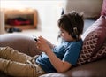 Child lying on couch wearing headphone listening to music, Kid sitting on sofa watching cartoons on tablet, Young boy playing game Royalty Free Stock Photo
