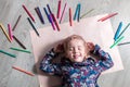 Child lying on the floor paper with closed eyes near crayons. Little girl painting, drawing. Top view. Creativity concept. Royalty Free Stock Photo