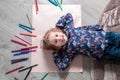 Child lying on the floor paper looking at the camera near crayons. Little girl painting, drawing. Top view. Creativity concept. Royalty Free Stock Photo