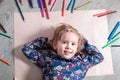 Child lying on the floor paper looking at the camera near crayons. Little girl painting, drawing. Top view. Creativity concept. Royalty Free Stock Photo