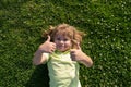 Child lying on grass. Kids with thumbs up sign, little boy portrait in summer nature park.