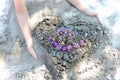 Child made a heart from sand and decorated with wildflowers, sunlight and sun glare