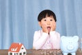 Child making faces in front of a pile of coins, a piggy bank and a house model Royalty Free Stock Photo