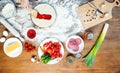 Child making pizza with pizza ingredients, tomatoes, salami and mushrooms on wooden tabletop