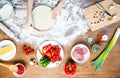 Child making pizza with pizza ingredients, tomatoes, salami and mushrooms on wooden tabletop