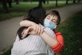 Child with medical mask hugging her mother with eyes closed