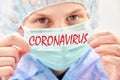 The child in a medical mask and safety cap on white background holding inscription Coronavirus. Closeup