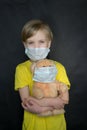 Child in a medical mask with a toy bear in his arms on a black background. The game of the doctor. The concept of