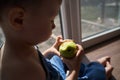 Child missing his mother concept. Little cute blond three year old boy sitting on windowsill touching window glass