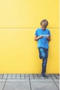 Child with mobile phone standing near yellow wall outside Royalty Free Stock Photo