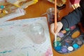 Child moistens the brush in a palette with multi-colored paints. Children`s creativity and painting science. Creative activity of