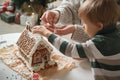 Little boy with mom decorating christmas gingerbread house together, family activities and traditions on Christmas and