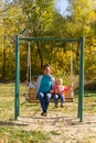 Child with mom ride on a swing in autumn