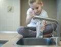 Child open water tap. Kitchen faucet. Glass of clean water. Pouring fresh drink. Hydration. Healthy lifestyle. Water quality check Royalty Free Stock Photo