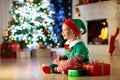 Child opening present at Christmas tree at home. Kid in elf costume with Xmas gifts and toys. Little baby boy with gift box and Royalty Free Stock Photo