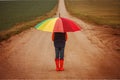 Child in orange rubber boots holding colorful umbrella under rain in autumn. Back view Royalty Free Stock Photo