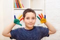 A child with painted colored fingers shows his hands sitting