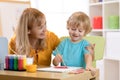 Child painting in preschool. Teacher help by little boy.