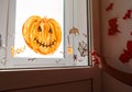 Child painting pumpkin on window preparing celebrate Halloween. Little kid draws decorates room interior with paper bats